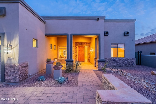 rear view of property featuring stone siding, fence, and stucco siding