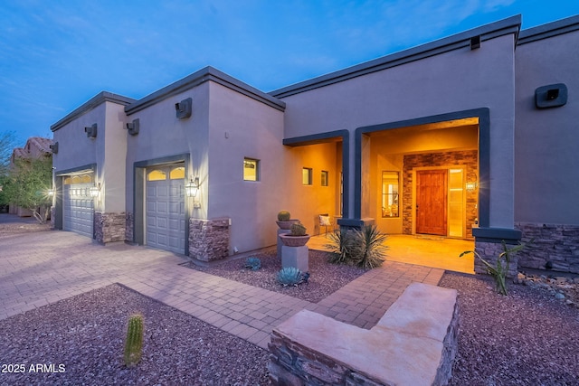 exterior space featuring decorative driveway, stone siding, an attached garage, and stucco siding