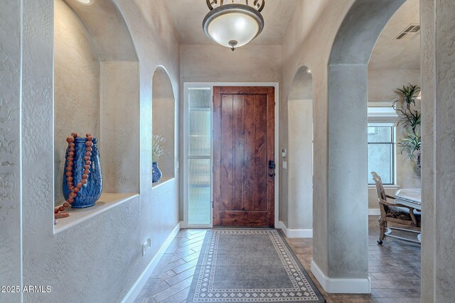 entryway featuring arched walkways, visible vents, a textured wall, and baseboards