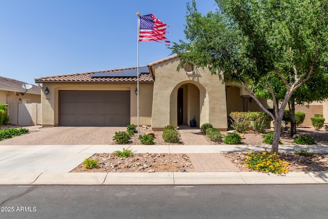 mediterranean / spanish-style home with stucco siding, decorative driveway, solar panels, a garage, and a tiled roof