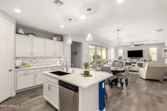 kitchen featuring stainless steel dishwasher, a sink, open floor plan, white cabinets, and light countertops