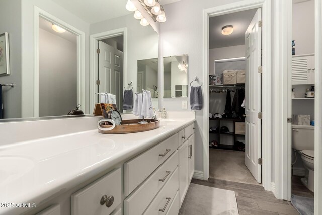 bathroom with toilet, double vanity, wood finished floors, and a walk in closet