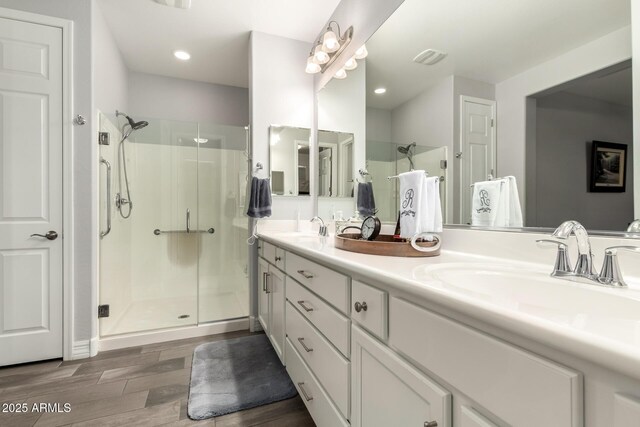 bathroom with a stall shower, wood finished floors, double vanity, and recessed lighting