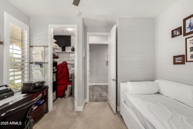 bedroom with a spacious closet, light carpet, a desk, a closet, and baseboards