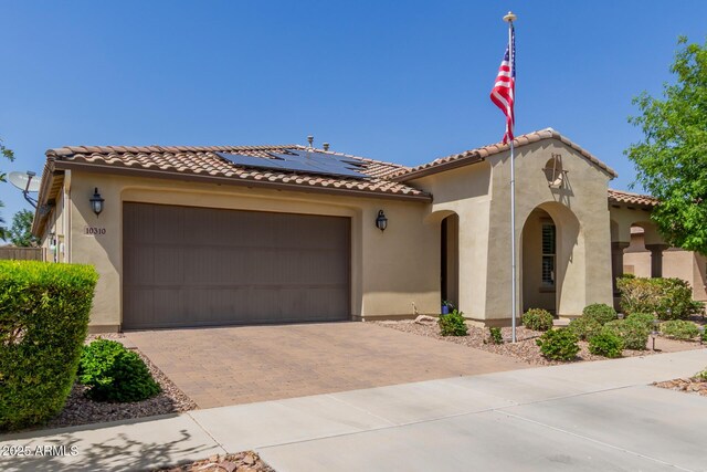 mediterranean / spanish-style home with decorative driveway, solar panels, stucco siding, an attached garage, and a tile roof