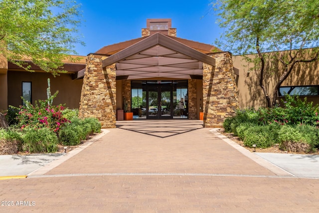 view of exterior entry featuring french doors, stucco siding, and stone siding