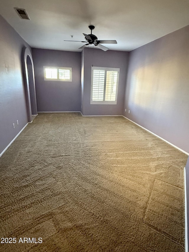 carpeted spare room featuring baseboards, ceiling fan, visible vents, and a healthy amount of sunlight