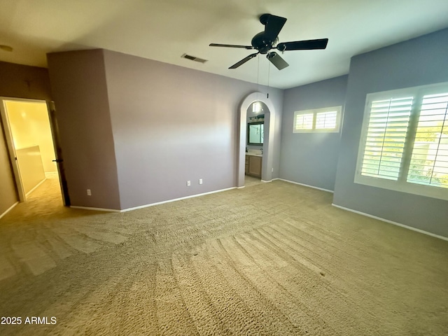 carpeted empty room with a ceiling fan, arched walkways, visible vents, and baseboards