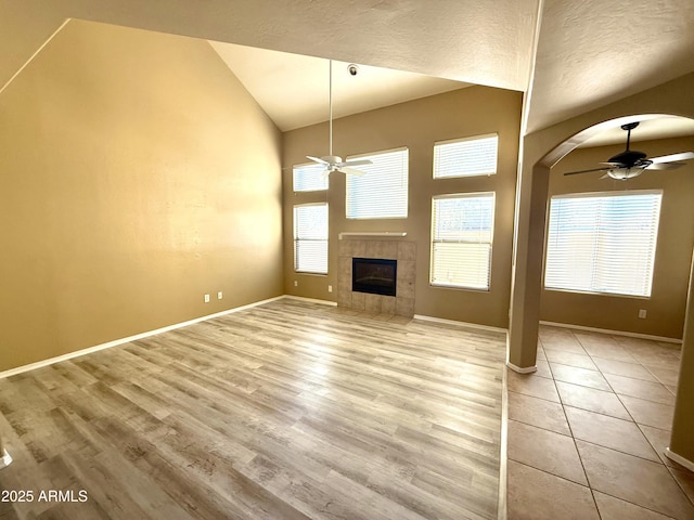 unfurnished living room featuring a ceiling fan, baseboards, a fireplace, and light wood finished floors