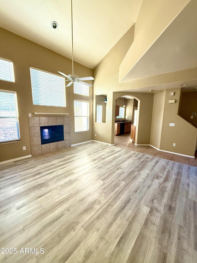 unfurnished living room with light wood-type flooring, high vaulted ceiling, a fireplace, and arched walkways