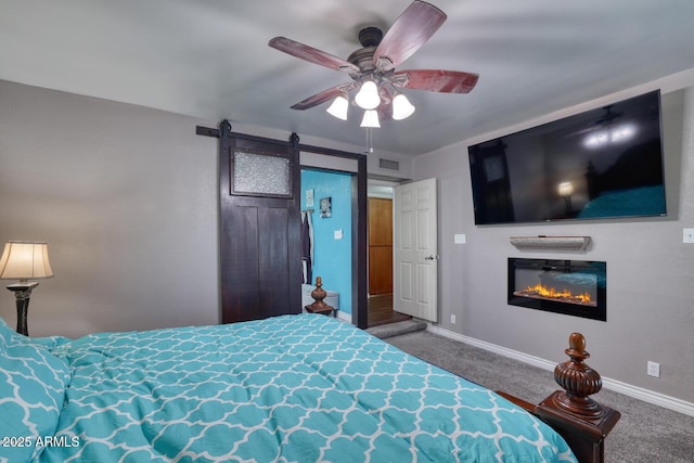 carpeted bedroom with ceiling fan, a barn door, a glass covered fireplace, baseboards, and visible vents