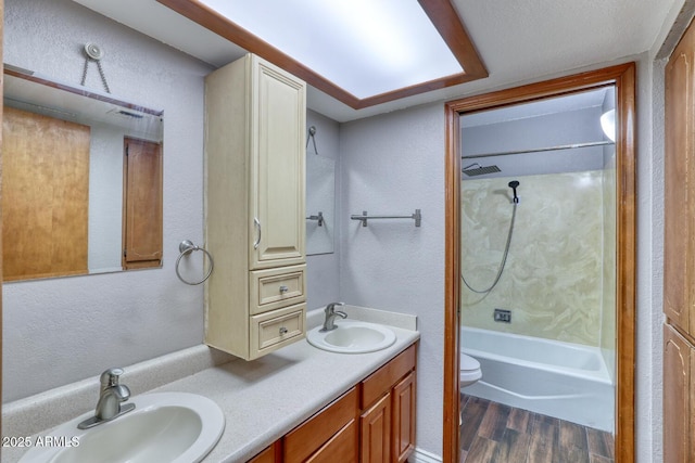 full bathroom with a textured wall, a sink, and wood finished floors