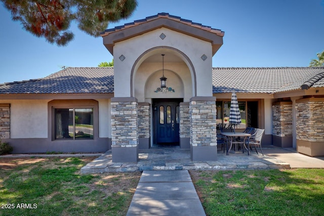 property entrance with a lawn, a tile roof, stone siding, and stucco siding