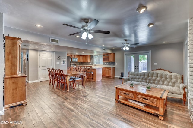 living area with baseboards, ceiling fan, visible vents, and wood finished floors