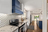 28422 N 32nd Ln, Phoenix, AZ 85083 - kitchen with electric stove, light stone countertops, blue cabinetry, wall chimney range hood, and white cabinetry