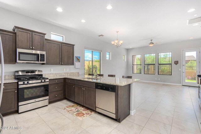 kitchen featuring dark brown cabinets, light stone counters, a breakfast bar area, kitchen peninsula, and appliances with stainless steel finishes