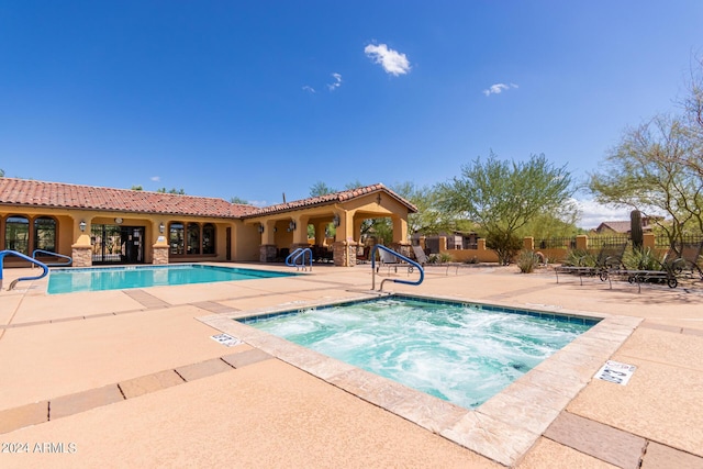 pool with a patio area, a community hot tub, and fence
