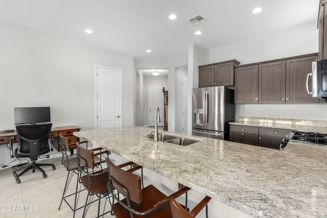 kitchen featuring visible vents, light stone counters, a sink, stainless steel appliances, and dark brown cabinets