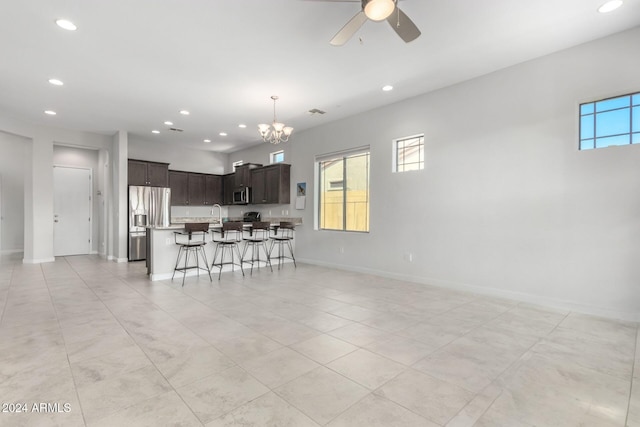 kitchen with a kitchen bar, ceiling fan with notable chandelier, open floor plan, appliances with stainless steel finishes, and dark brown cabinets
