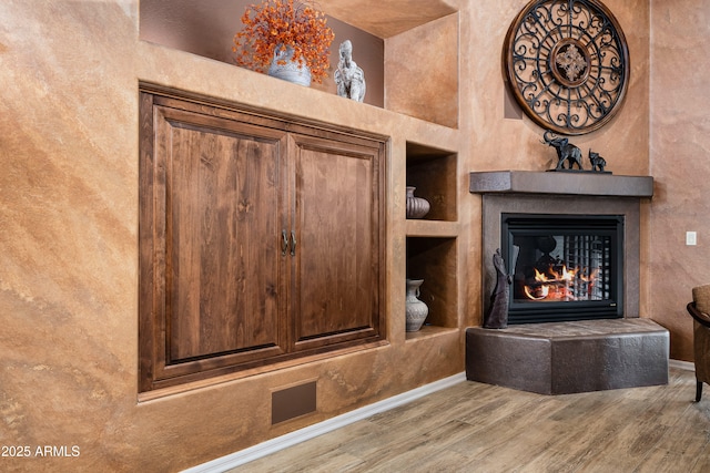 details featuring a tiled fireplace, baseboards, and wood finished floors