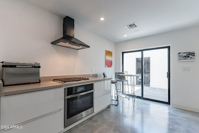 kitchen featuring wall chimney range hood, stainless steel appliances, and white cabinets