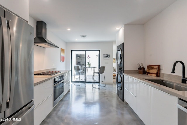 kitchen featuring stainless steel appliances, sink, wall chimney range hood, and white cabinetry