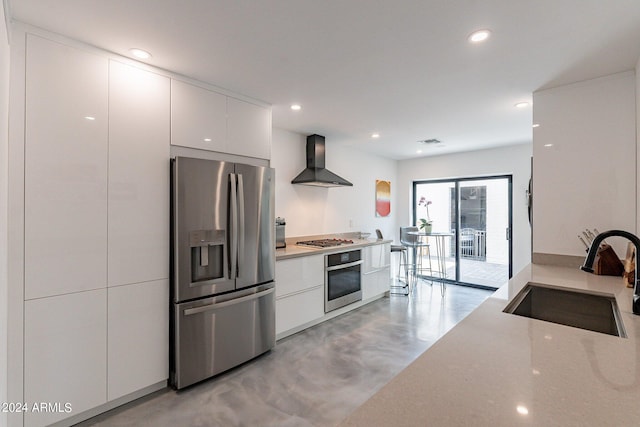 kitchen featuring wall chimney exhaust hood, white cabinetry, sink, and stainless steel appliances