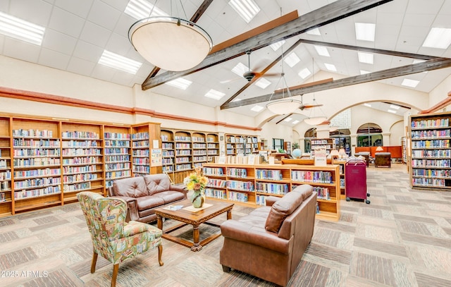 sitting room with beam ceiling, carpet flooring, wall of books, and high vaulted ceiling