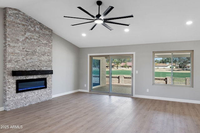 unfurnished living room with baseboards, lofted ceiling, a stone fireplace, and wood finished floors