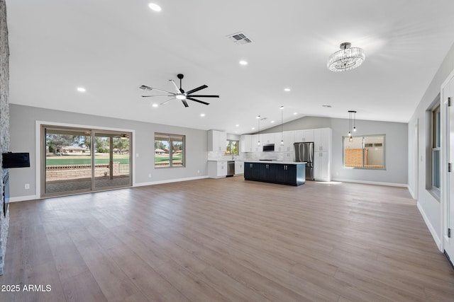 unfurnished living room featuring light wood-type flooring, visible vents, ceiling fan with notable chandelier, and vaulted ceiling