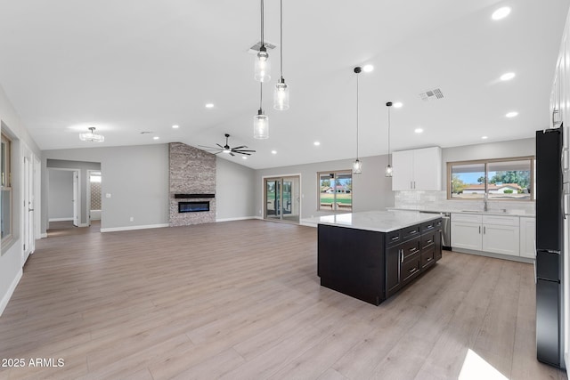 kitchen featuring visible vents, a sink, white cabinets, a fireplace, and lofted ceiling