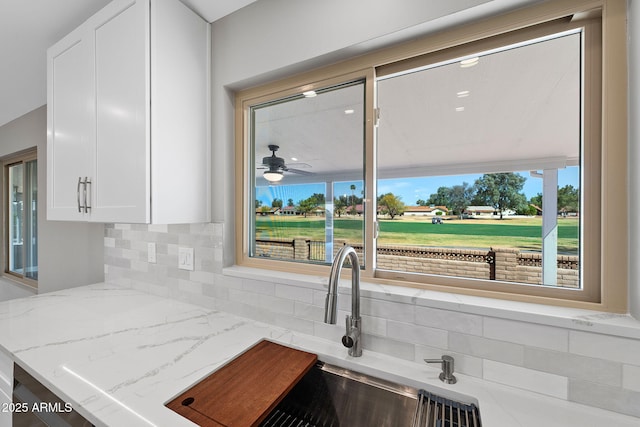 kitchen featuring white cabinets, light stone counters, backsplash, and a sink