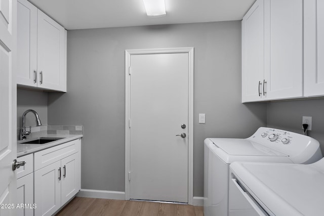 washroom with a sink, cabinet space, light wood-style floors, separate washer and dryer, and baseboards