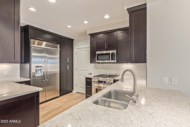 kitchen with light wood-type flooring, dark brown cabinetry, light stone countertops, sink, and high end appliances