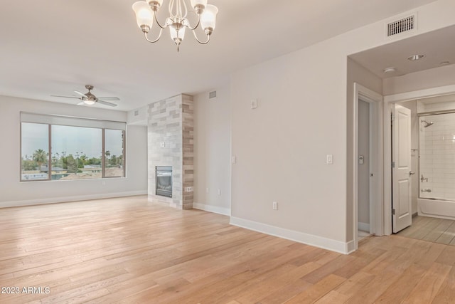unfurnished living room with light wood-style flooring, a chandelier, a tile fireplace, ceiling fan, and baseboards
