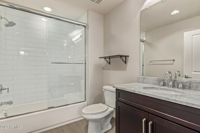 full bathroom with hardwood / wood-style floors, shower / bath combination with glass door, toilet, and vanity