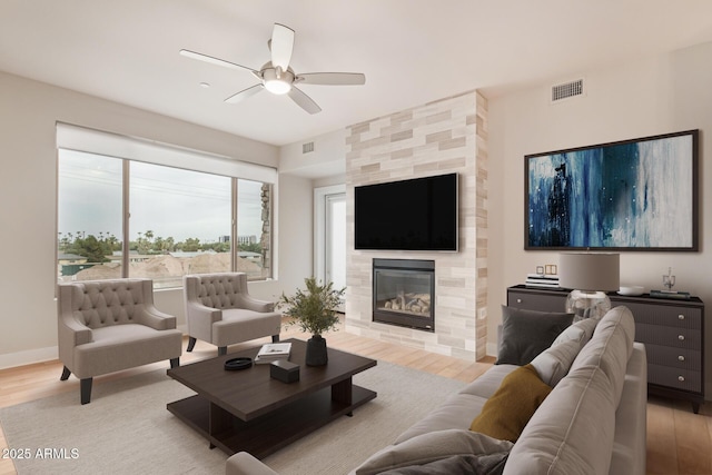 living area with wood finished floors, a ceiling fan, a tiled fireplace, and baseboards