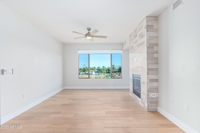 unfurnished living room featuring light wood-type flooring, a large fireplace, and ceiling fan