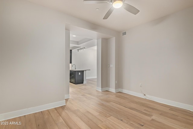 spare room with ceiling fan, light wood-style flooring, baseboards, and a sink