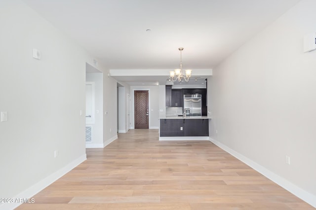 unfurnished dining area with a chandelier, light wood-style floors, baseboards, and a sink
