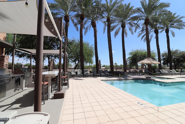 community pool with a bar, area for grilling, a patio area, and a grill