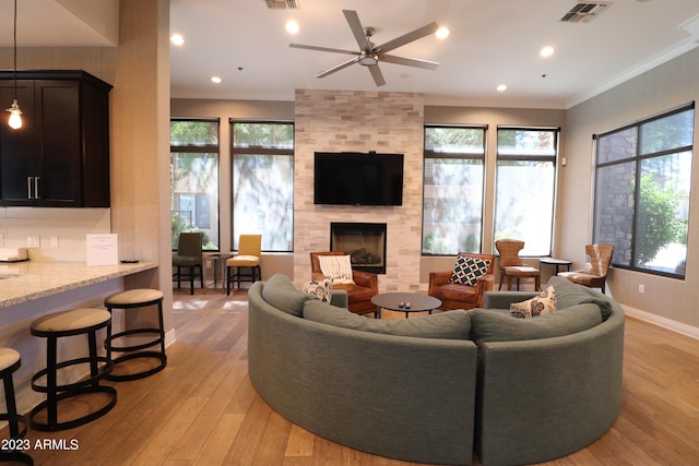 living room with a tiled fireplace, a healthy amount of sunlight, light wood-type flooring, and crown molding