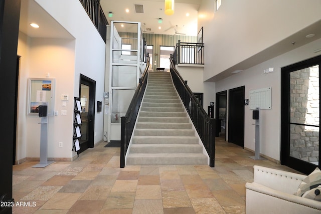 stairway featuring a high ceiling, stone tile flooring, baseboards, and recessed lighting