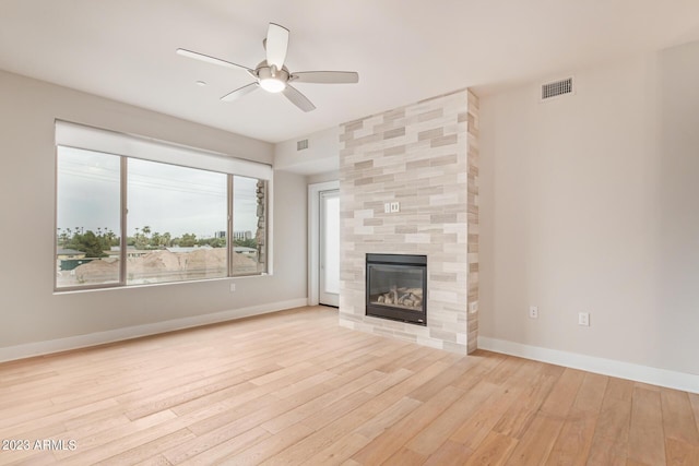 unfurnished living room with a ceiling fan, light wood-type flooring, a tile fireplace, and baseboards