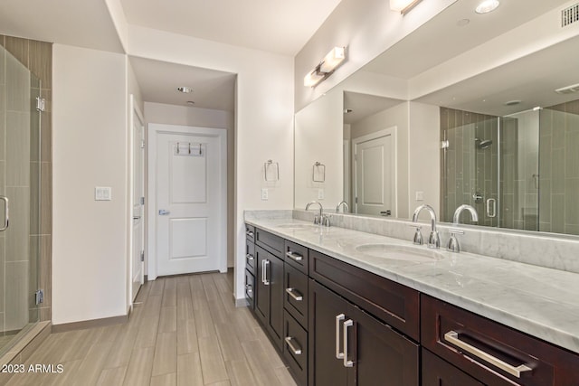 bathroom featuring a shower stall, double vanity, baseboards, and wood finished floors