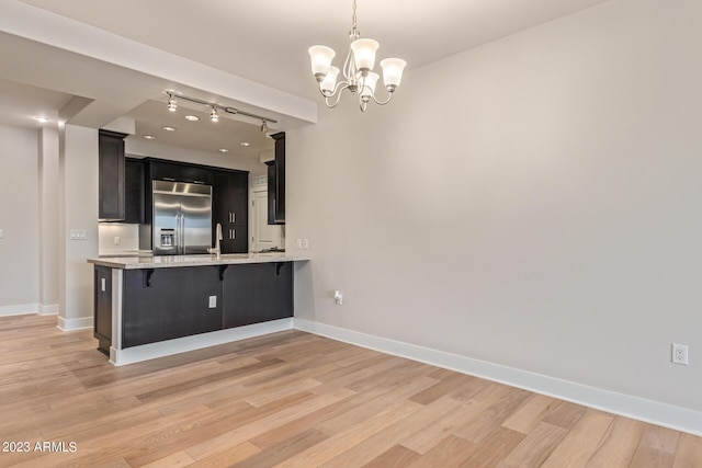 kitchen featuring built in refrigerator, a kitchen breakfast bar, light wood finished floors, dark cabinets, and a chandelier