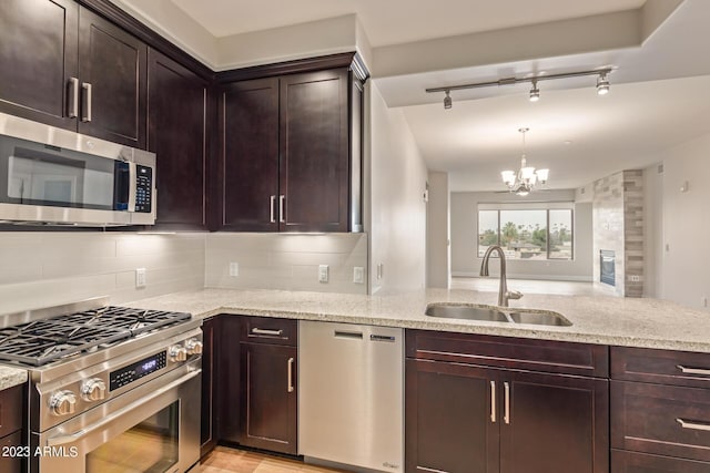 kitchen featuring stainless steel appliances, a sink, a chandelier, and light stone countertops