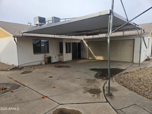 back of house featuring brick siding, central AC unit, concrete driveway, and roof with shingles