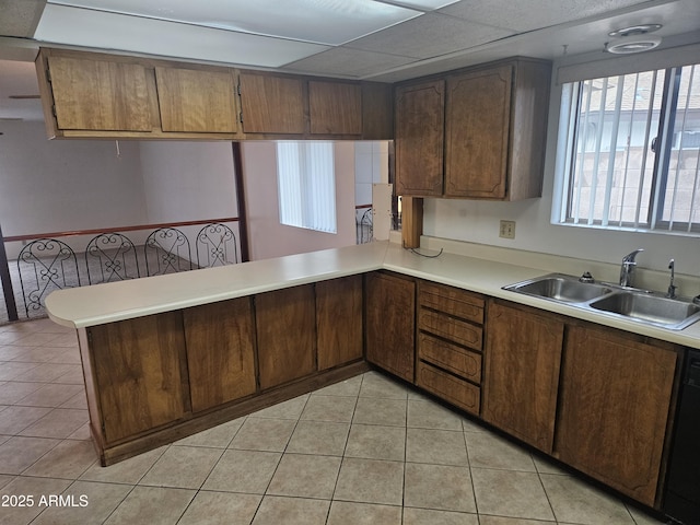 kitchen with a sink, a peninsula, light tile patterned flooring, light countertops, and dishwasher