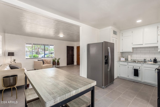 kitchen with light stone counters, stainless steel fridge, backsplash, white cabinetry, and tile patterned floors